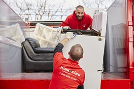 Two Junk King professionals loading a washing machine onto a truck bed.